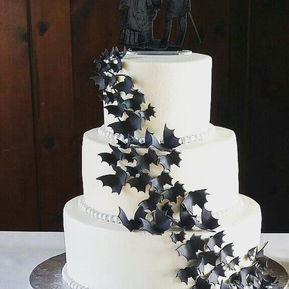 a three tiered cake decorated with black bats and a figurine on top