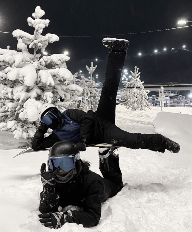 two snowboarders are doing tricks in the snow at night, one is upside down