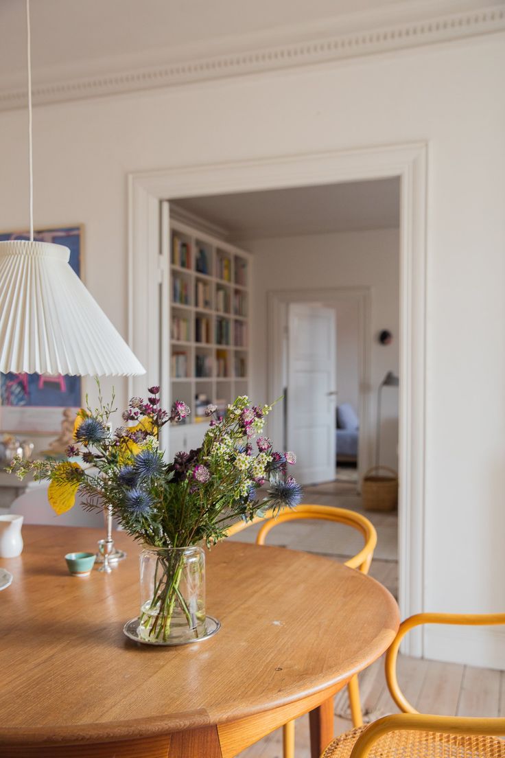 a vase with flowers sitting on top of a wooden table next to two yellow chairs