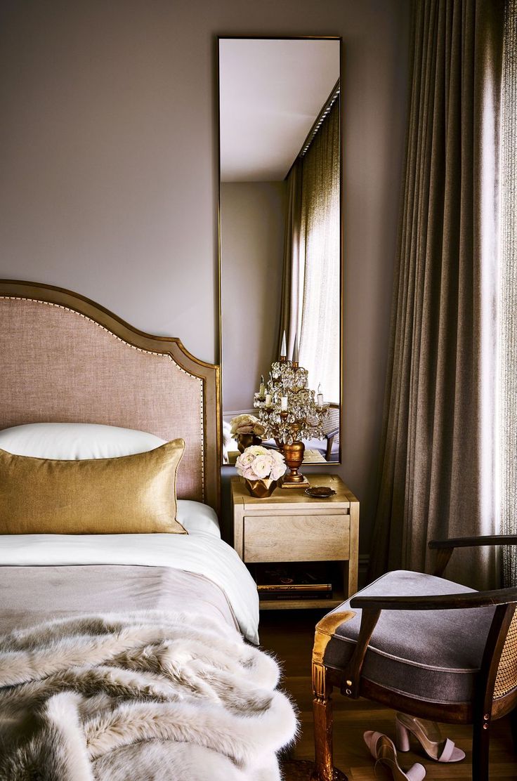 a bedroom with a bed, mirror and chair in the corner next to a window