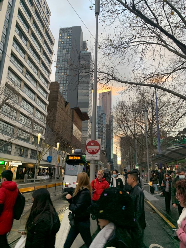 many people are walking down the street in front of tall buildings and trees with no leaves on them