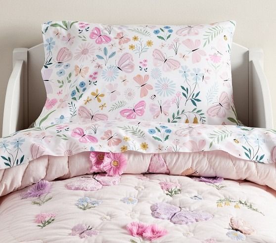 a bed with pink and blue flowers on the comforter next to a white headboard