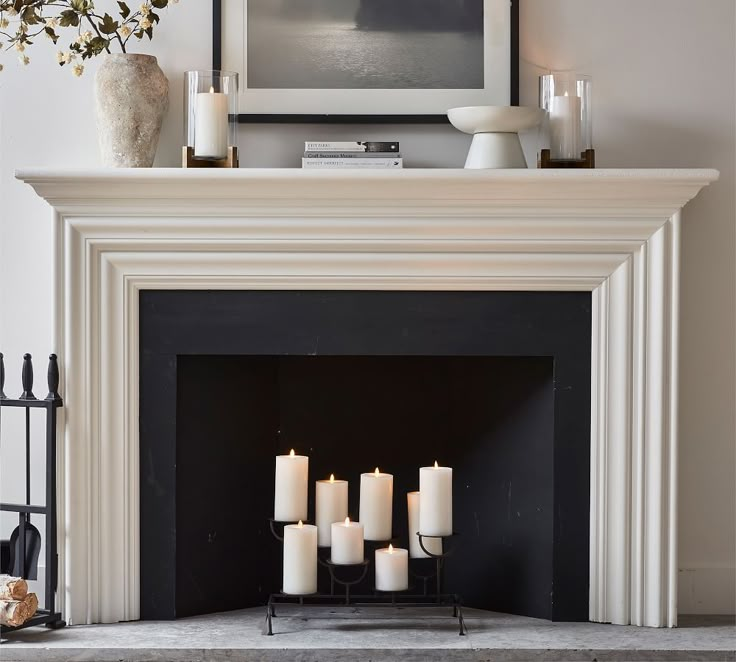 a fireplace with white candles in front of it and a painting on the wall above