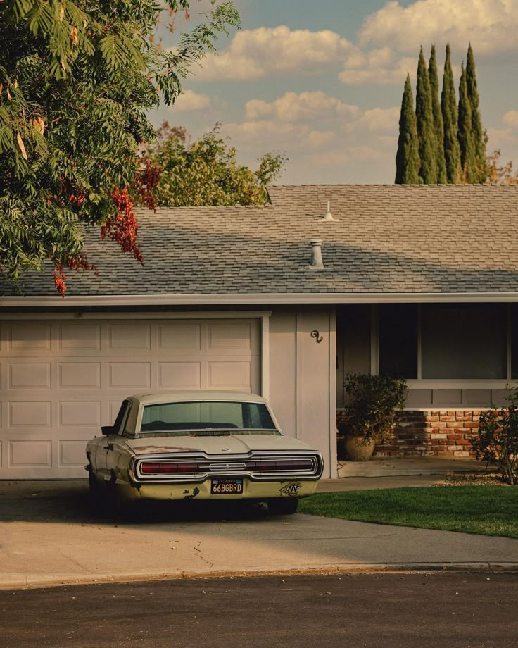 an old car parked in front of a house with trees and bushes around it's driveway