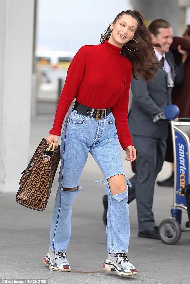 a woman in red sweater and ripped jeans walking down the street with her handbag