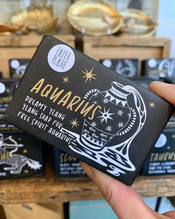 a person holding up a black and white box with gold foil on it that says aquarius