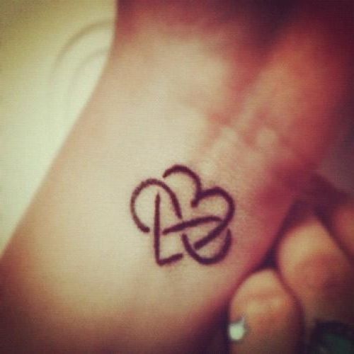 a small tattoo on the wrist of a woman's left hand, with two intertwined hearts