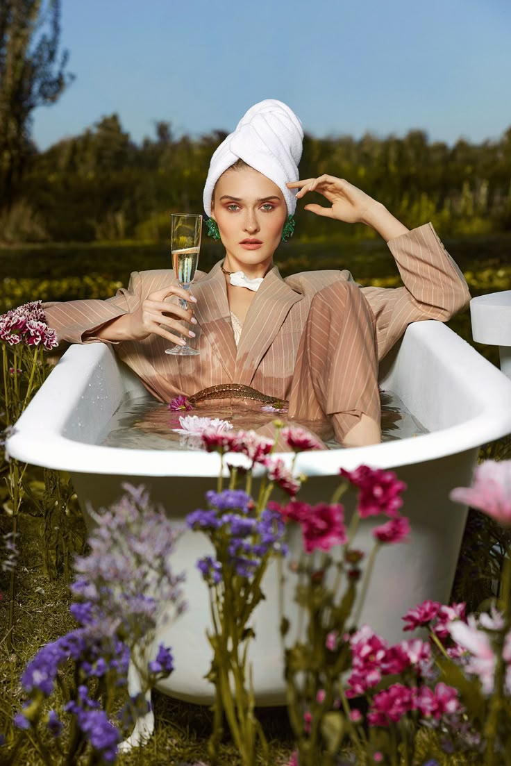 a woman in a bathtub surrounded by flowers and holding a glass with her hand