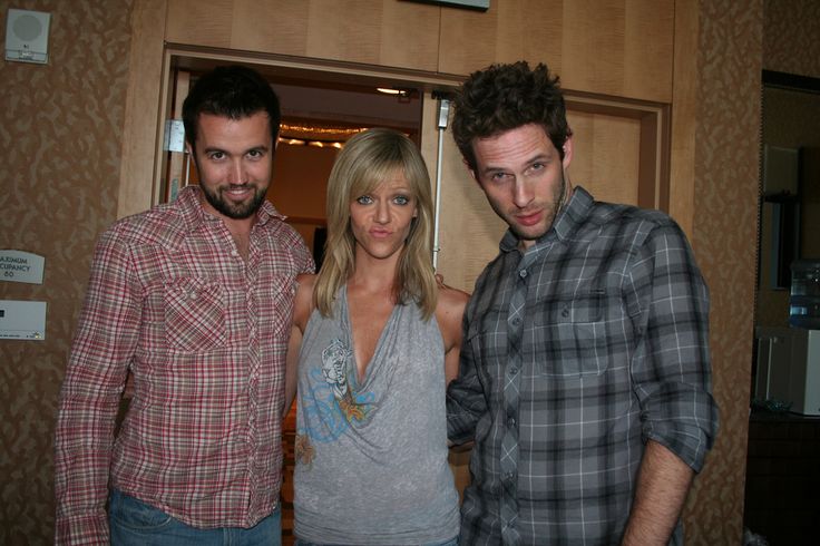 two men and a woman standing next to each other in front of an open door