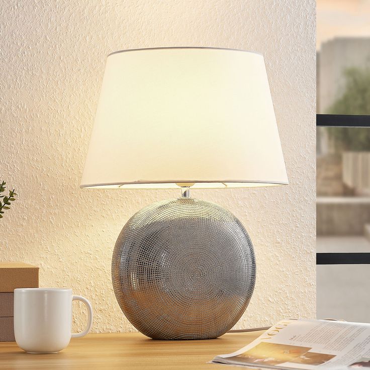 a table lamp sitting on top of a wooden desk next to a cup and book