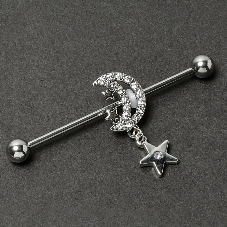 Product Details14 Gauge Clear CZ Gem Moon Dangle Star Industrial Barbell 38mm Give your industrial piercing a look as lovely as the night sky with this 14 gauge helix barbell. It is made with a 1 1/2 inch 316L surgical grade stainless steel straight barbell with 5mm ball ends. It features a crescent moon charm, embellished along the edge with clear cubic zirconia gems and tiny stars. Dangling beneath is another star with a clear cubic zirconia gem at the center. You can even slide it up and down Moon Industrial Piercing, Cute Industrial Piercing Jewelry, Industrial Bar Piercing, Industrial Piercing Jewelry, Conch Piercing Jewelry, Opal Nose Ring, Daith Piercing Jewelry, Tragus Piercing Jewelry, Pregnancy Belly Rings