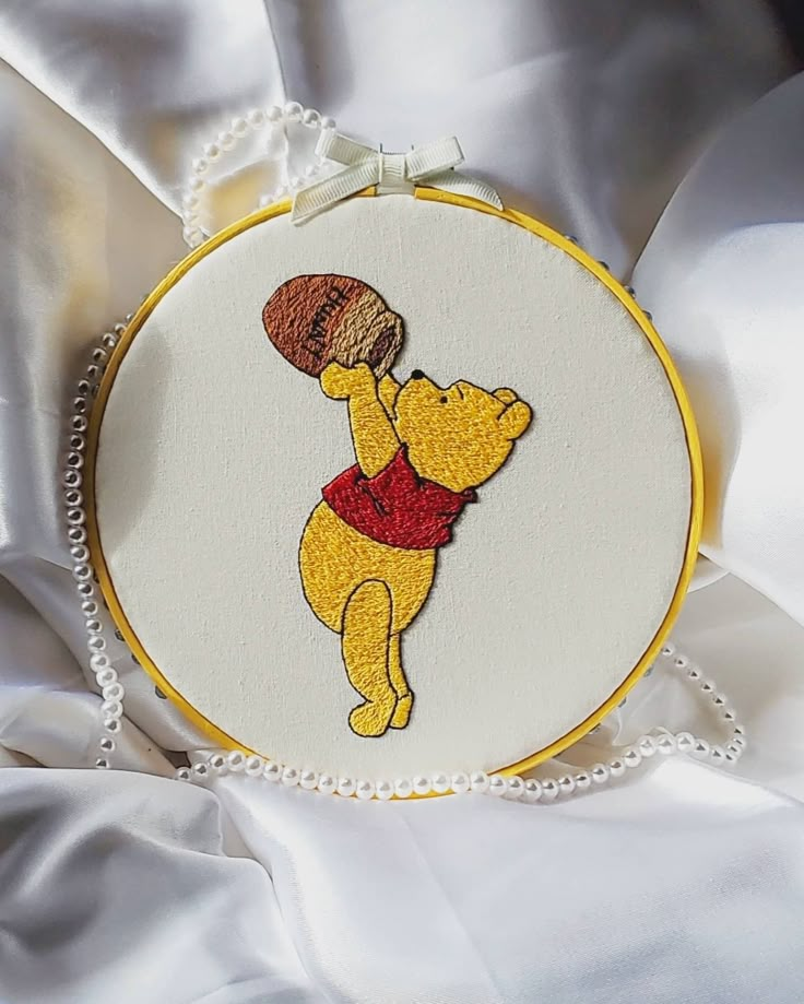 a winnie the pooh embroideryed on a white fabric with pearls around it's edge