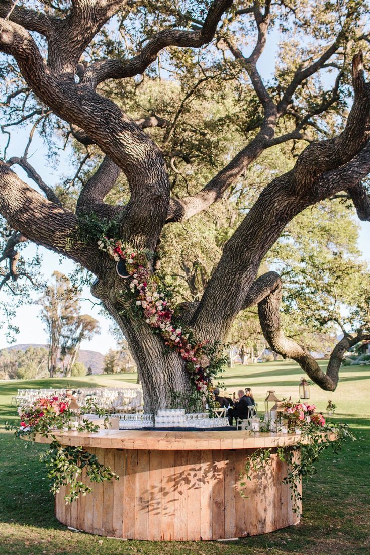 an outdoor ceremony setup under a tree with flowers and greenery on the top table