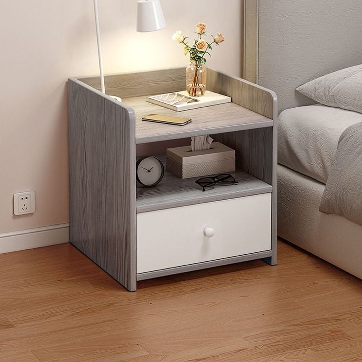 a nightstand with a lamp on top of it next to a bed