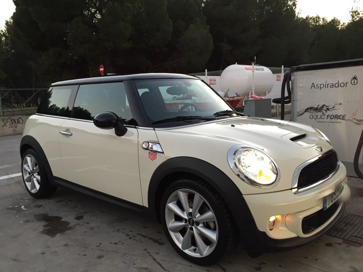 a small white car parked in a parking lot next to a gas pump and trees