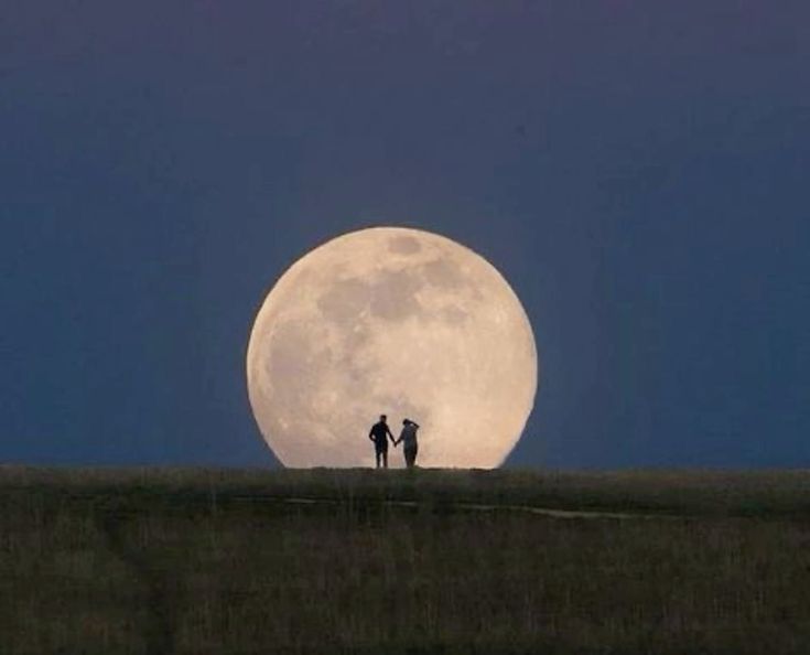 two people standing on top of a hill under a full moon