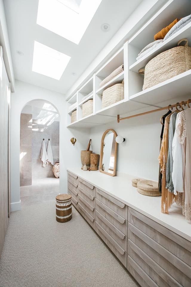 a walk in closet filled with lots of clothes and baskets on top of wooden shelves