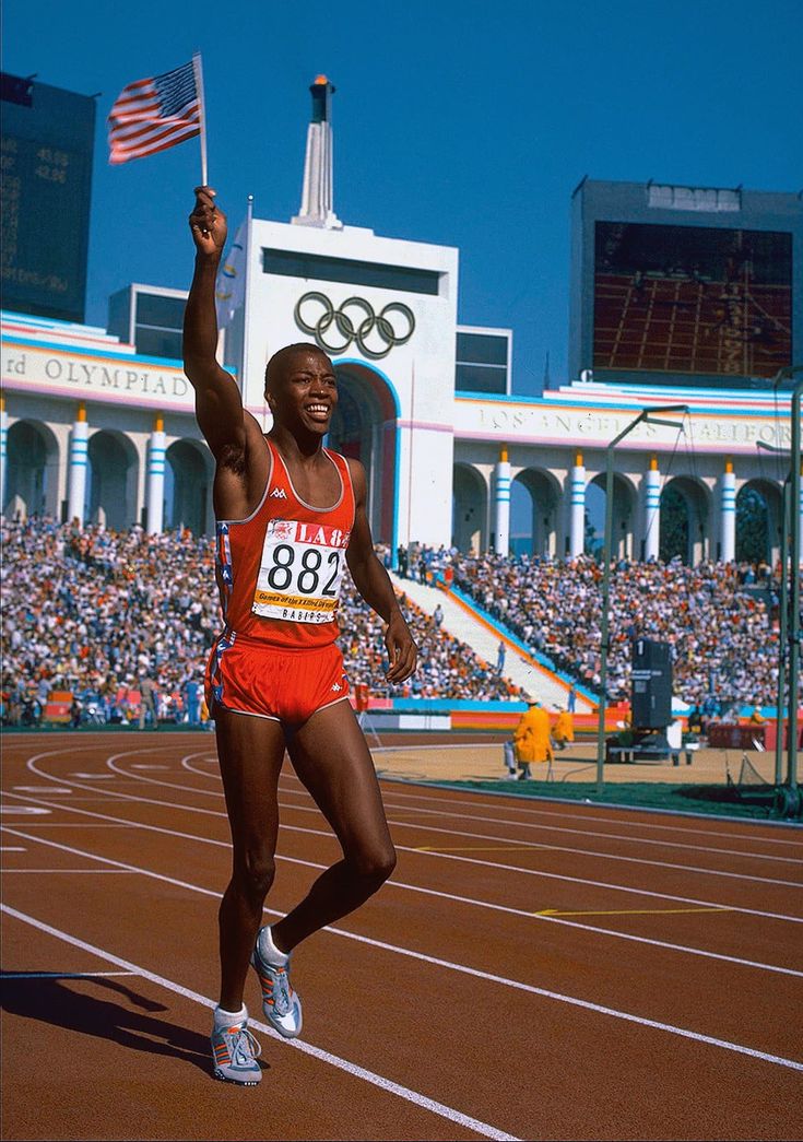 a man in an orange shirt and red shorts is running on a track with his hand up