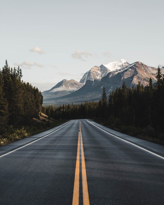 an empty road with mountains in the background and trees on both sides that are yellow