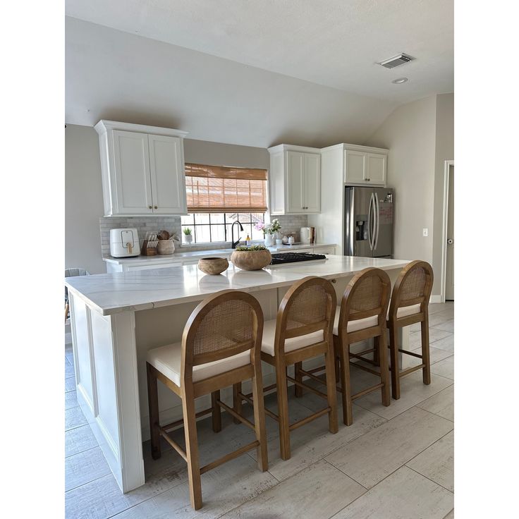 a kitchen island with four chairs and a refrigerator in the backround next to it