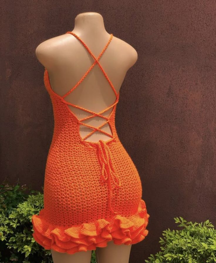 an orange crochet swimsuit on display in front of a brown wall and bushes