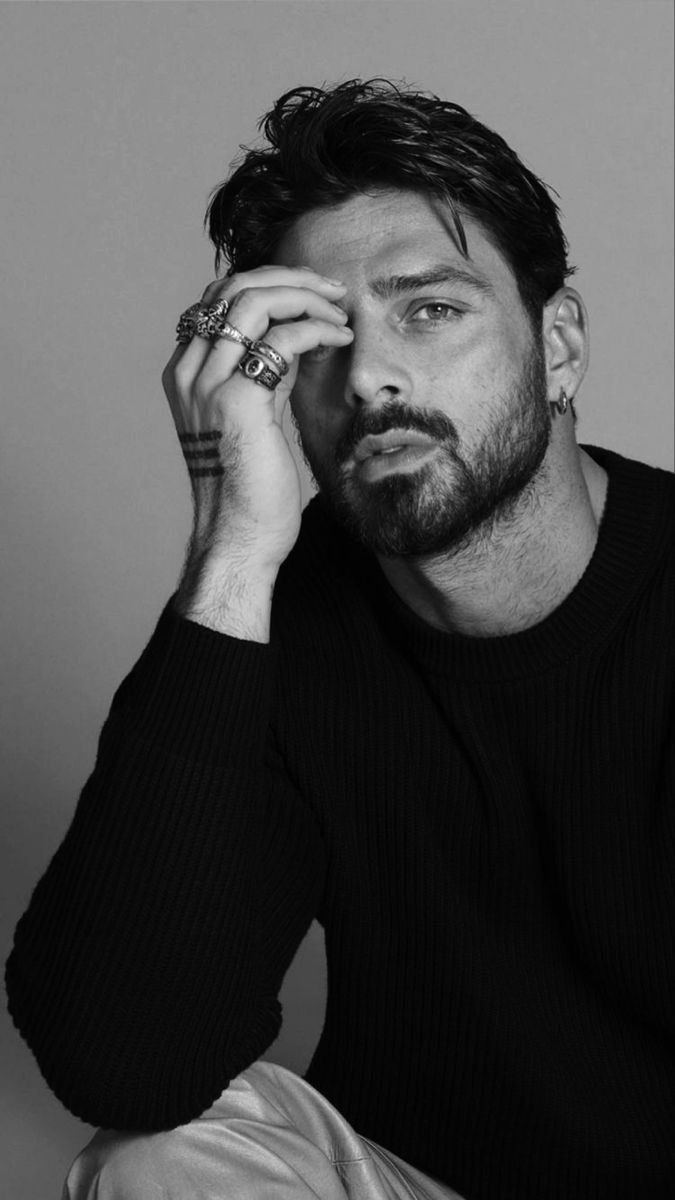 a man sitting down with his hand on his head and looking at the camera while wearing a black sweater