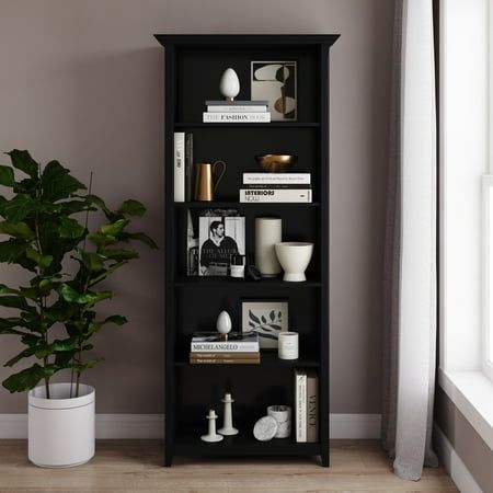 a black book shelf with books and other items on it next to a potted plant