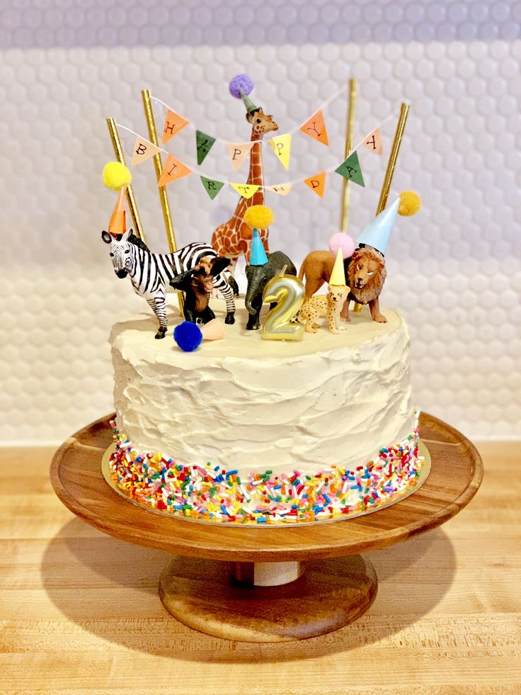 a birthday cake decorated with animals and flags on a wooden stand in front of a wall