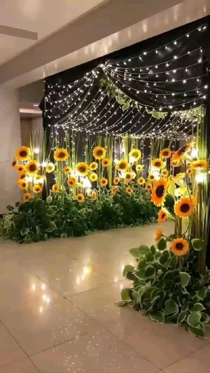 sunflowers and greenery are arranged in the middle of an indoor area with string lights