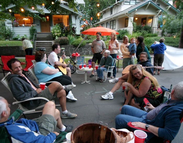 a group of people sitting on lawn chairs in front of a house with an open fire pit