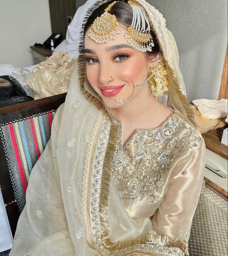 a woman in a white and gold bridal outfit with her hair styled up to the side