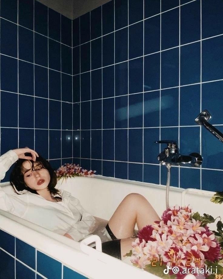 a woman laying in a bathtub with flowers on the side and blue tiled walls