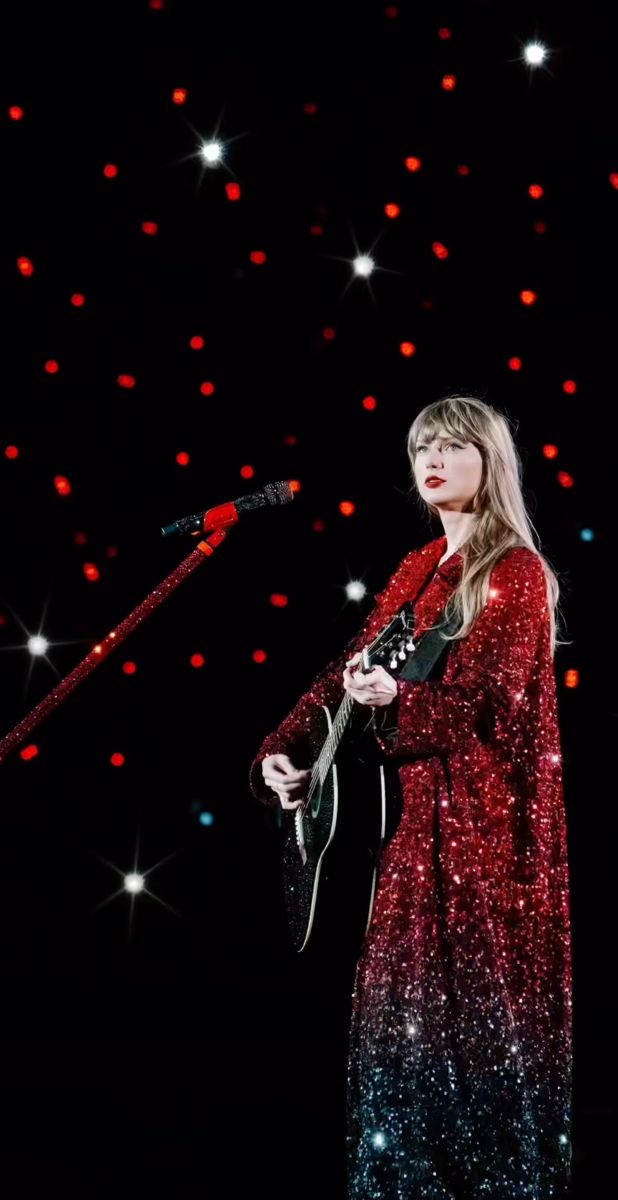 a woman in a red dress is holding a guitar and singing into a microphone on stage