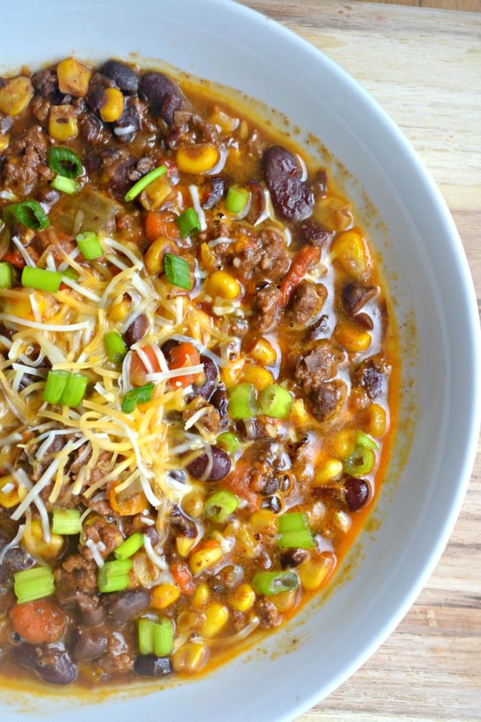 a white bowl filled with chili, corn and cheese on top of a wooden table