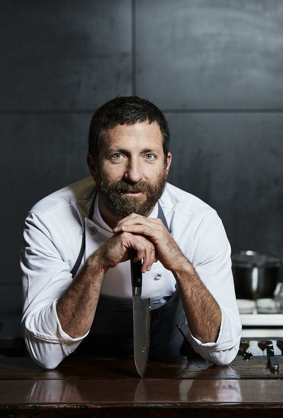 a man leaning on a table with a knife in front of him and looking at the camera