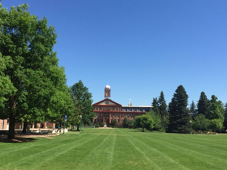 a large building with a clock tower in the middle of a green field next to trees