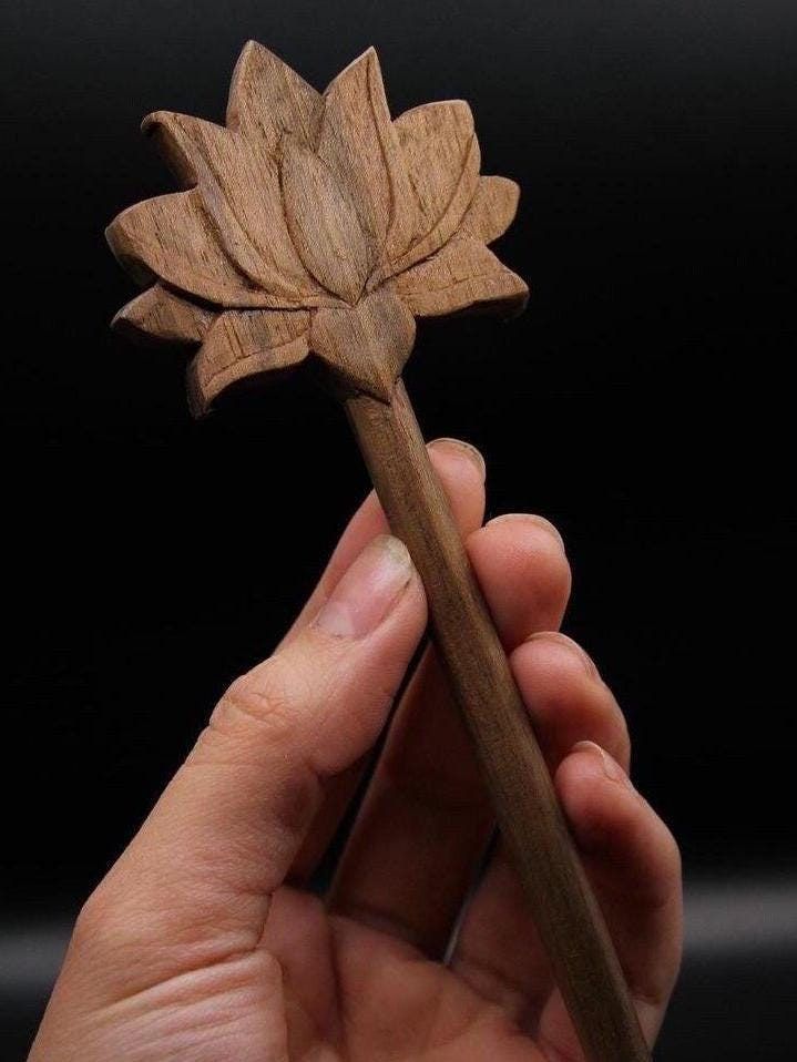 a hand holding a wooden stick with a flower on it