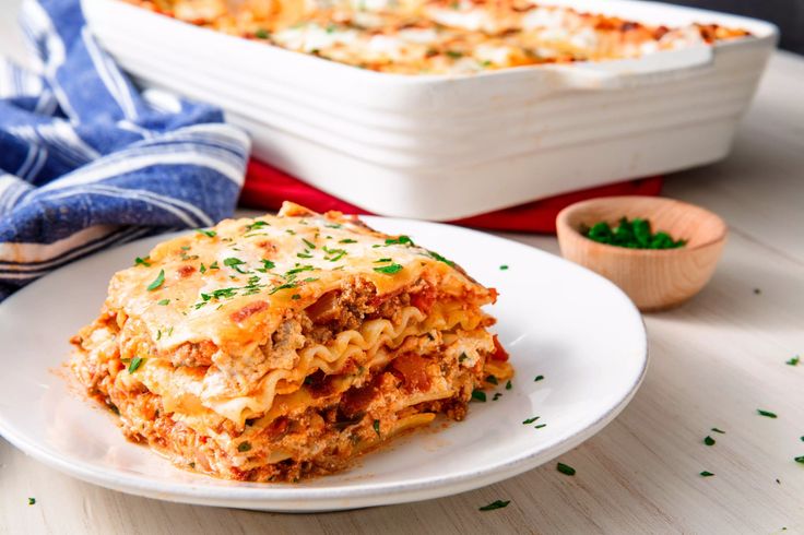 a white plate topped with lasagna next to a casserole dish