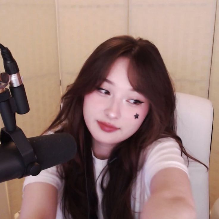 a woman with long hair sitting in a chair next to a microphone and looking at the camera