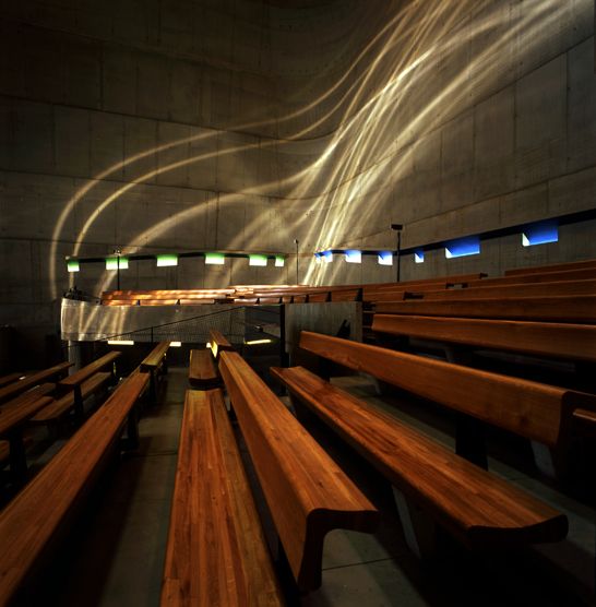 several wooden benches are lined up in a room with concrete walls and lights on the ceiling