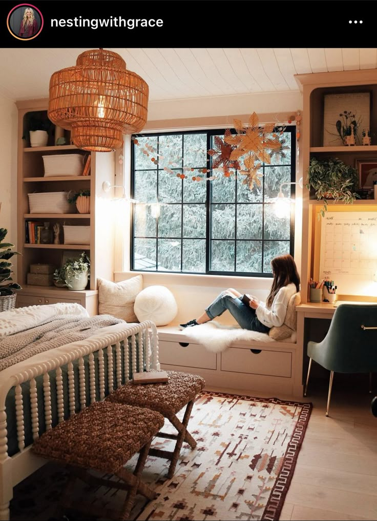 a woman sitting on a bed in a room with a large window and rugs