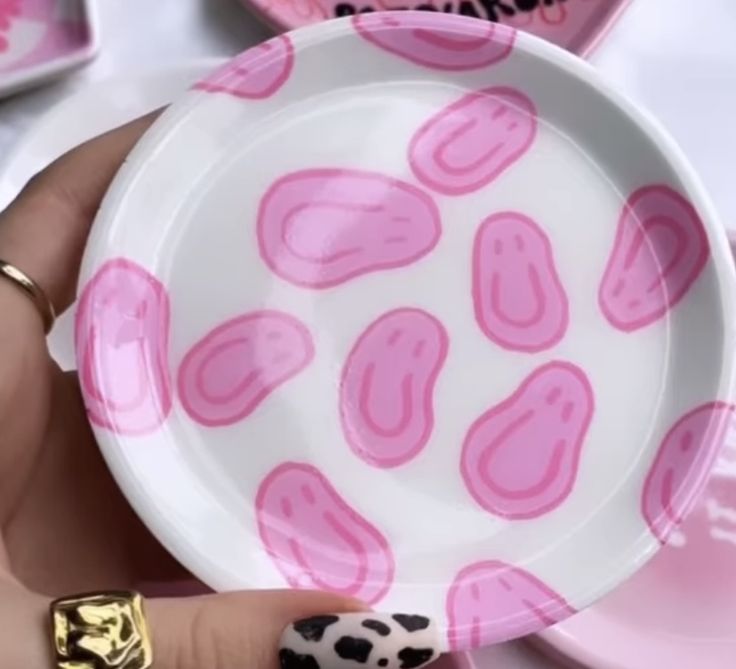 a hand holding a pink and white plate with black spots on it, in front of other plates