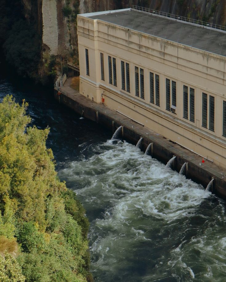 a large building sitting on the side of a river next to a bridge with water coming out of it