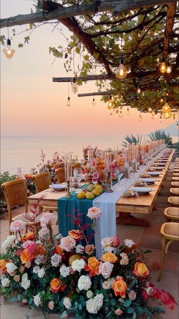 an outdoor dining table set up with flowers and candles on the table for dinner by the ocean