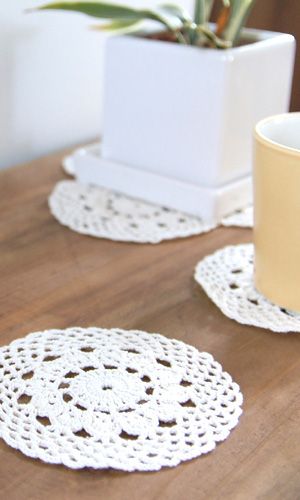 two crocheted doily coasters sitting on a table next to a plant