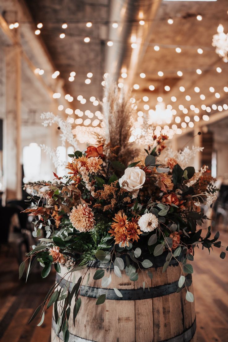 a wooden barrel with flowers and greenery on it in a room filled with lights