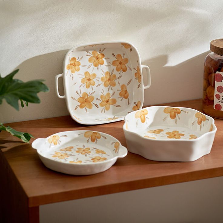 three white dishes sitting on top of a wooden table next to a potted plant