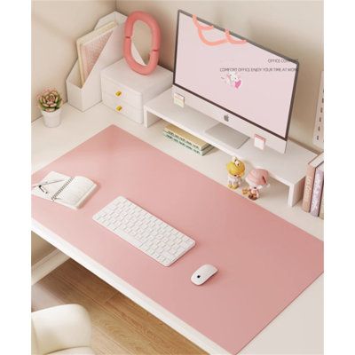 a computer desk with a pink mouse pad and keyboard on it, next to a monitor