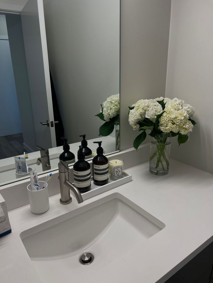 a bathroom sink with soap, lotion and flowers in the vase next to it