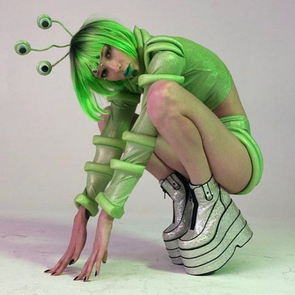 a woman with green hair is bent over wearing silver shoes and holding her leg in the air